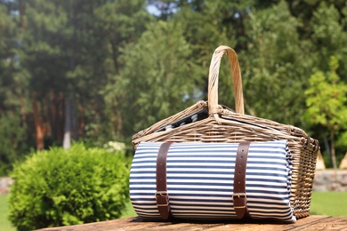 Photo of Picnic basket with blanket on wooden table in garden