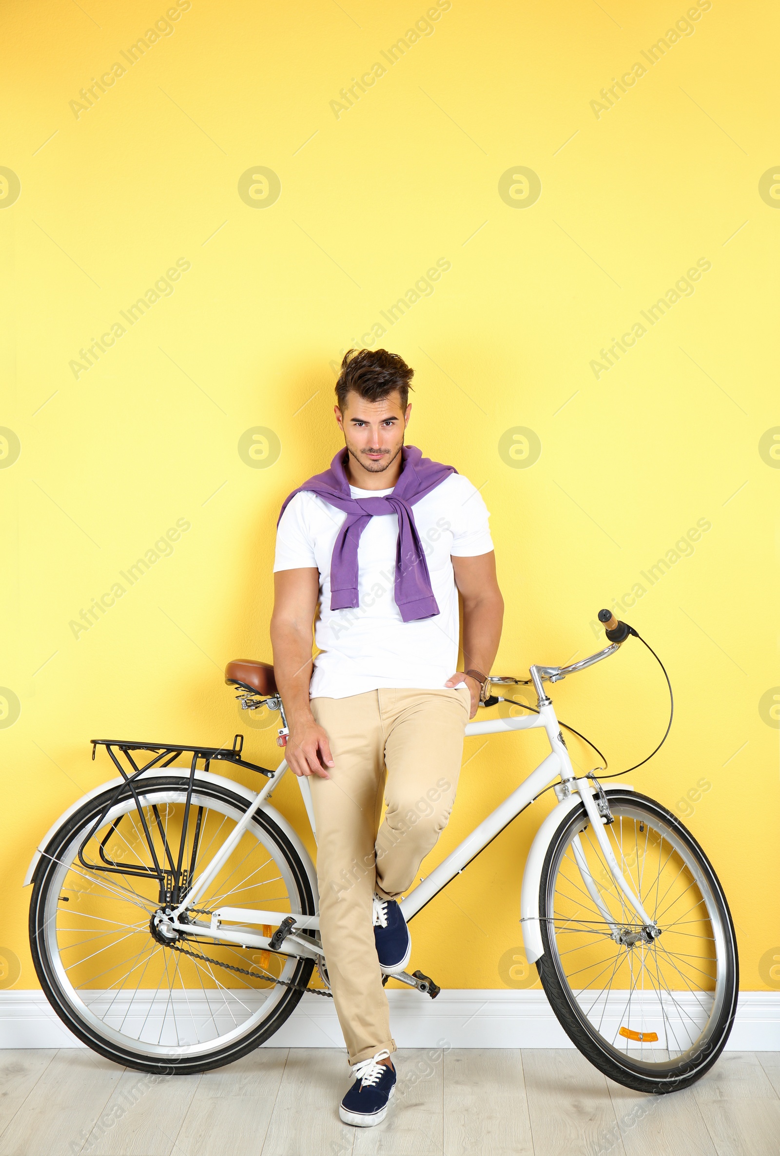 Photo of Handsome young hipster man with bicycle near yellow wall