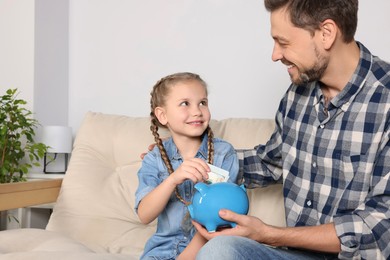 Photo of Little girl with her father putting money into piggy bank at home
