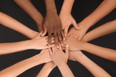 Photo of Group of multiracial people joining hands together on black background, closeup