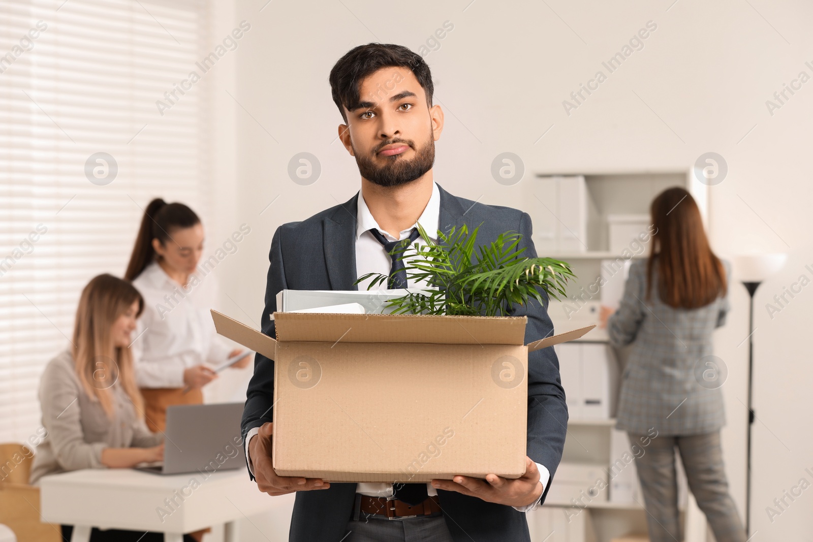 Photo of Unemployment problem. Frustrated man with box of personal belongings in office