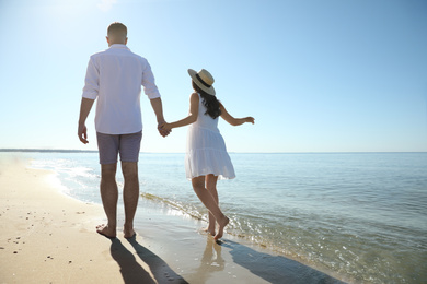Happy young couple walking on beach near sea. Honeymoon trip