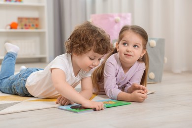 Photo of Cute little children reading book on floor in kindergarten