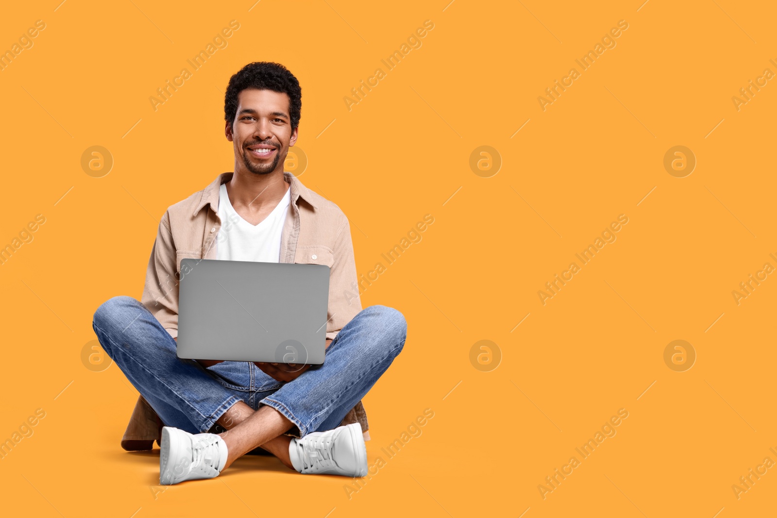 Photo of Happy man using laptop against orange background. Space for text