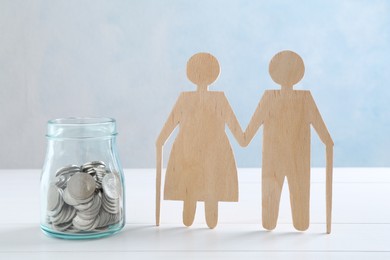 Photo of Pension savings. Figure of senior couple and jar of coins on white wooden table