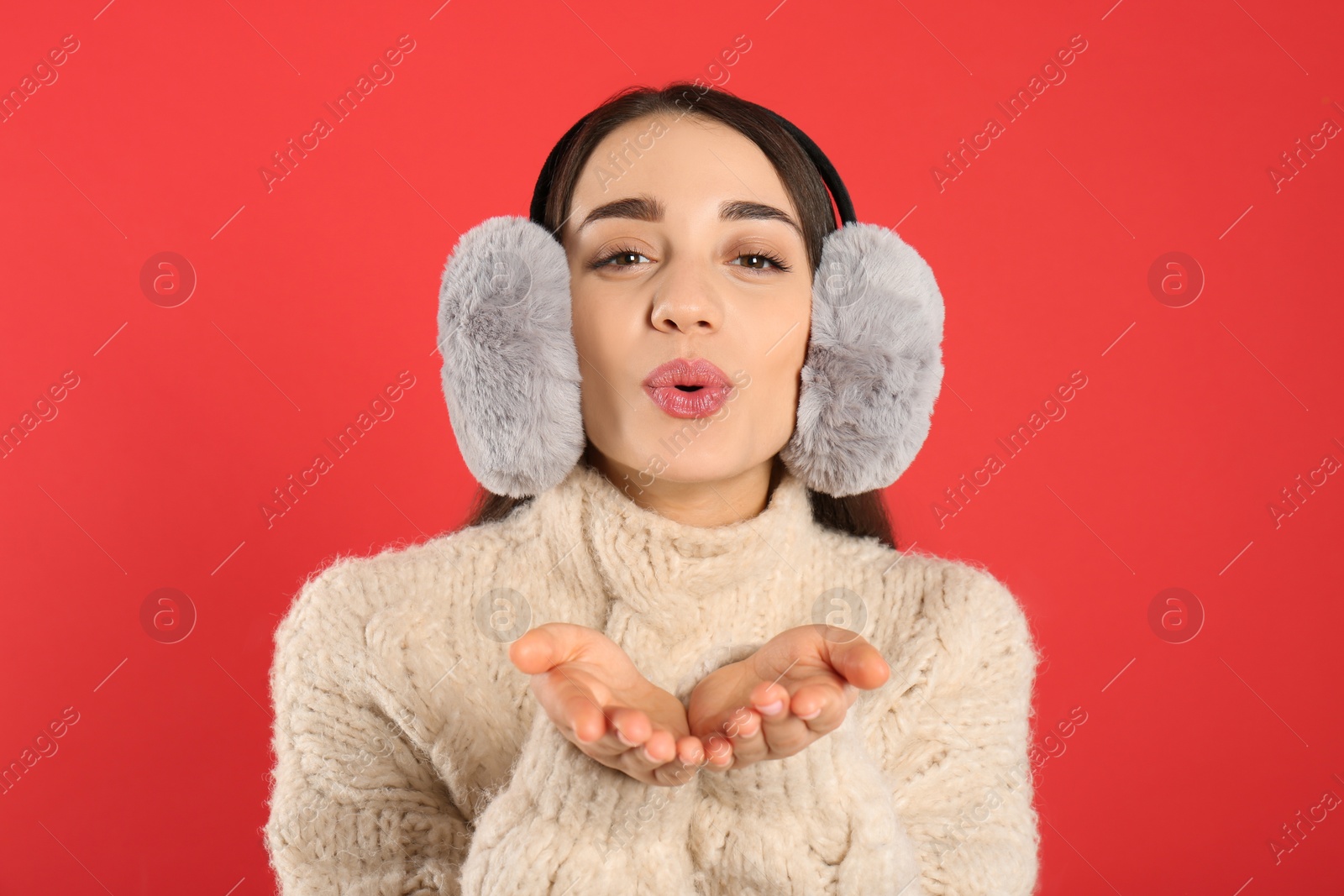 Photo of Beautiful young woman wearing earmuffs on red background