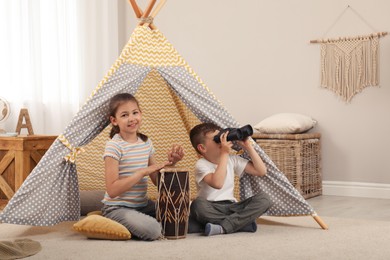 Photo of Cute little children playing in toy wigwam at home
