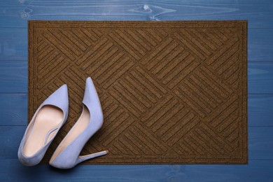 Photo of New clean door mat with shoes on blue wooden floor, top view