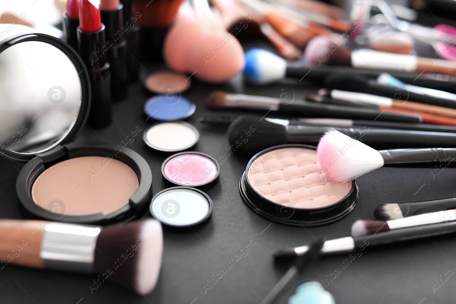 Photo of Different makeup brushes and cosmetic products on black background