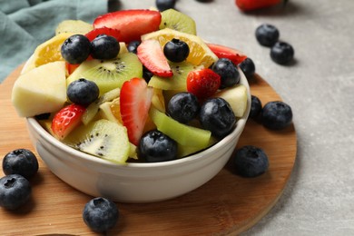 Photo of Tasty fruit salad in bowl and ingredients on gray table, closeup