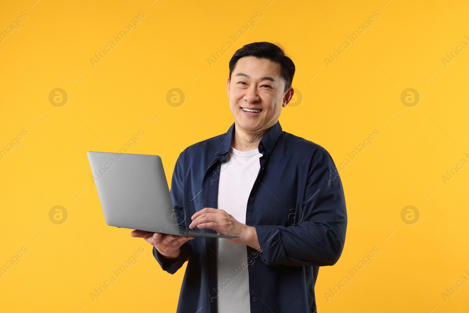 Photo of Portrait of happy man with laptop on yellow background