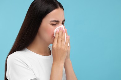 Photo of Suffering from allergy. Young woman blowing her nose in tissue on light blue background. Space for text
