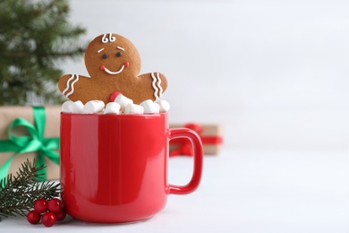 Photo of Gingerbread man in red cup with marshmallows on white table, space for text