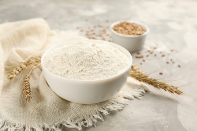 Photo of Bowl of flour and wheat ears on light grey table