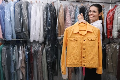 Photo of Dry-cleaning service. Happy worker holding hanger with jacket indoors, space for text