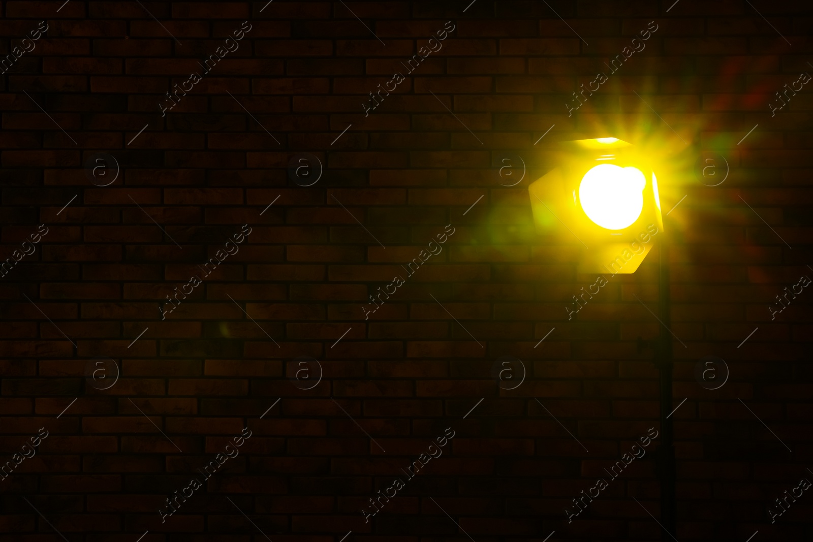 Photo of Bright yellow spotlight near brick wall in darkness, space for text