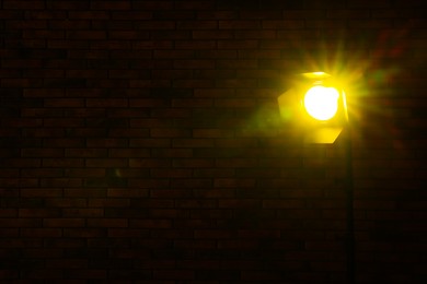 Photo of Bright yellow spotlight near brick wall in darkness, space for text