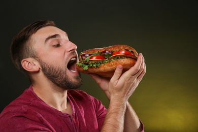 Photo of Young man eating tasty burger on color background