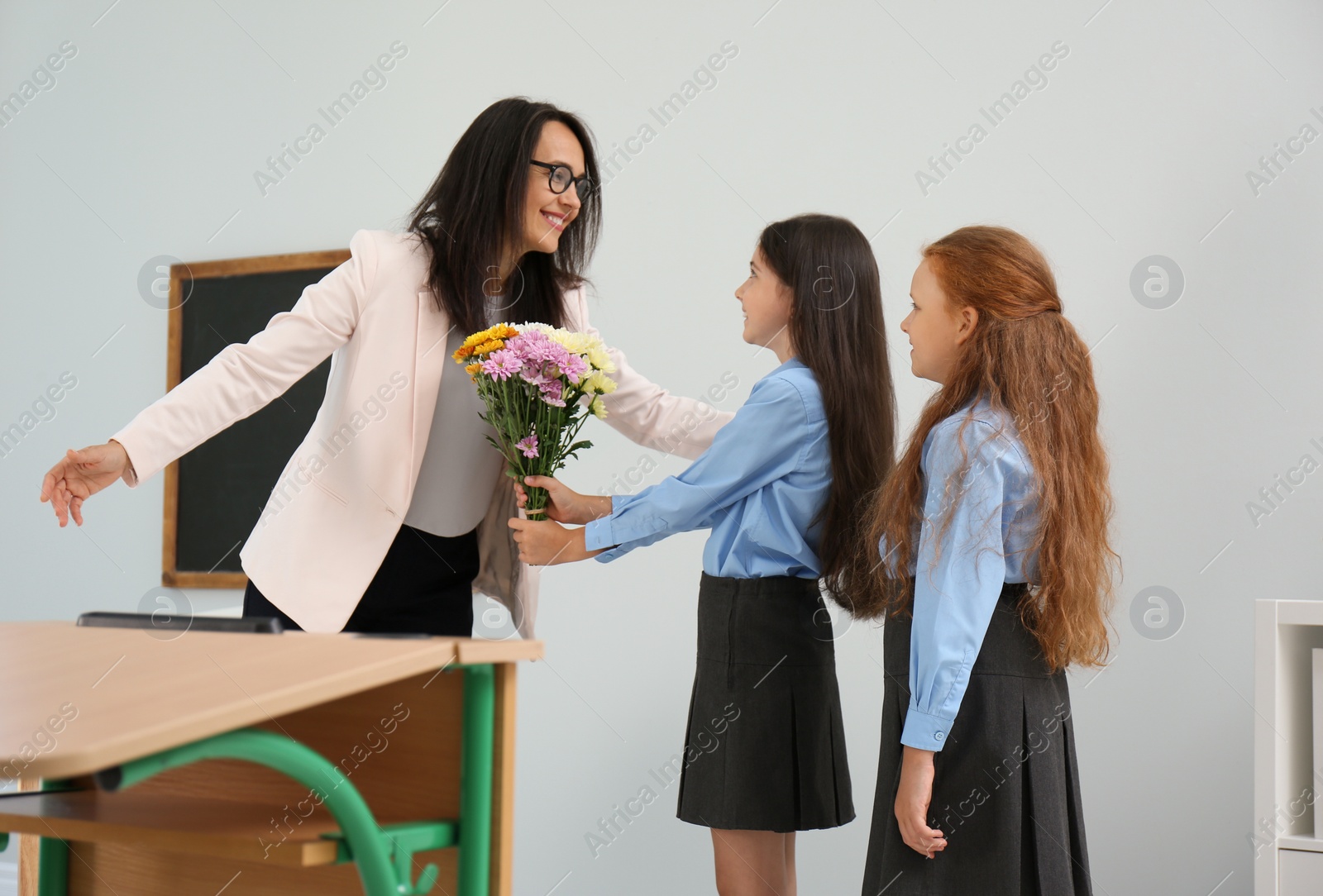 Photo of Schoolgirls with bouquet congratulating their pedagogue in classroom. Teacher's day