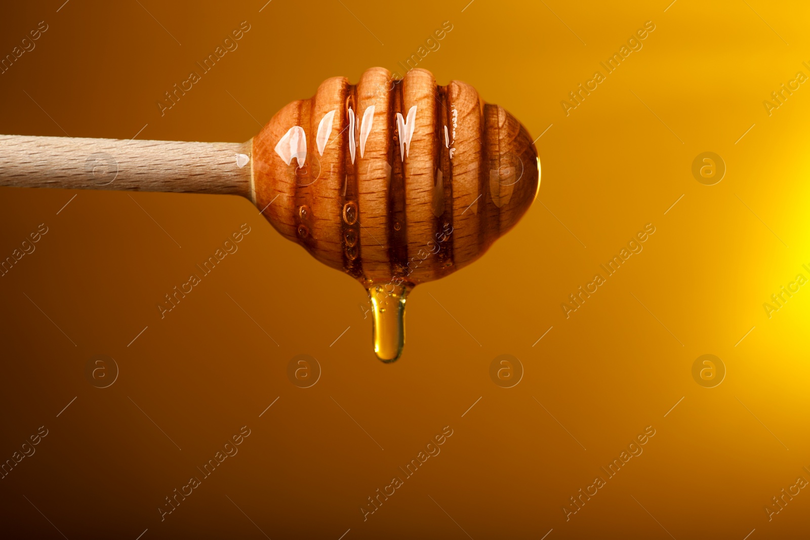 Photo of Pouring honey from dipper against golden background, space for text