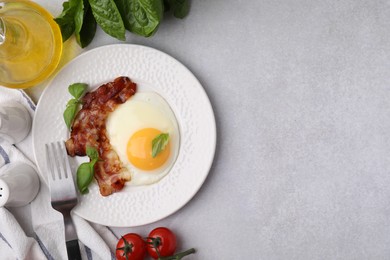 Fried egg and bacon served on light grey table, top view. Space for text
