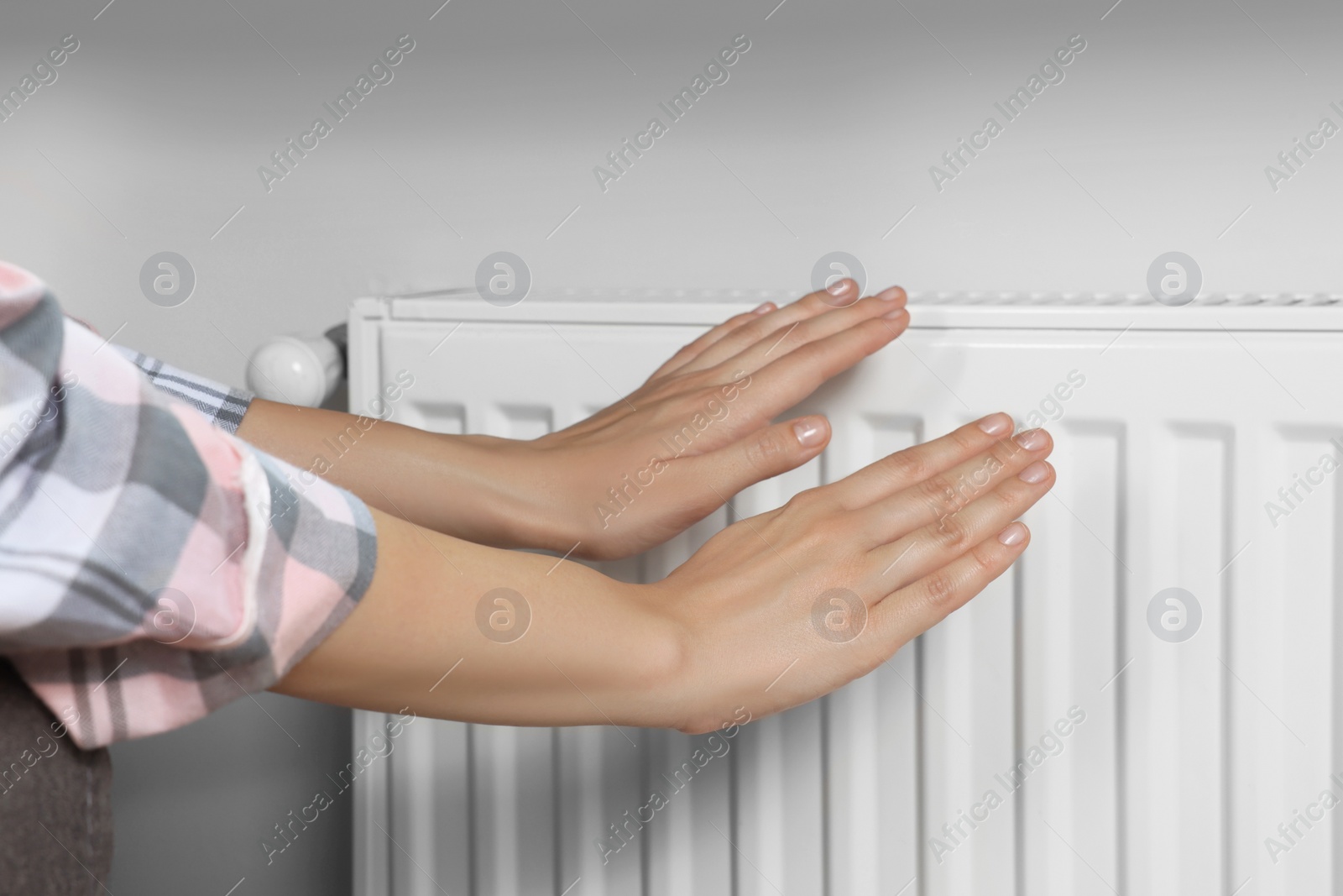 Photo of Woman warming hands on heating radiator near white wall, closeup