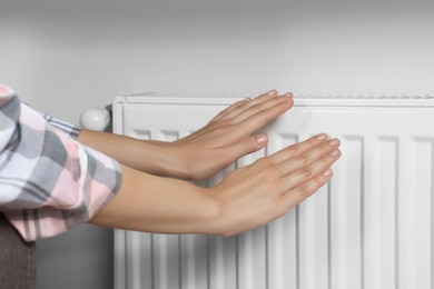 Photo of Woman warming hands on heating radiator near white wall, closeup