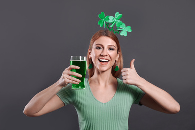 Photo of Young woman with clover headband and green beer on grey background. St. Patrick's Day celebration