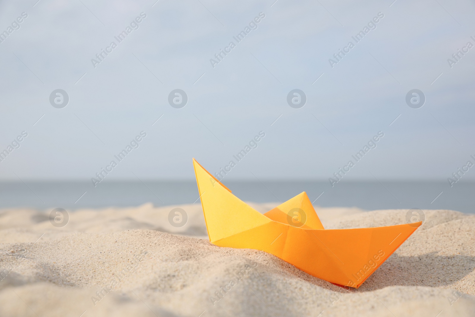 Photo of Orange paper boat on sandy beach near sea, space for text