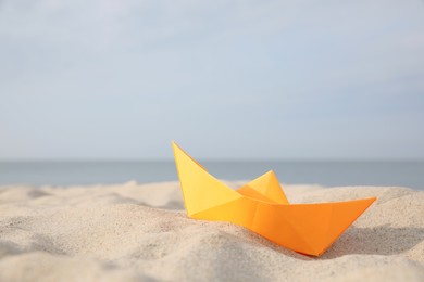 Orange paper boat on sandy beach near sea, space for text