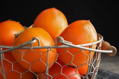 Photo of Delicious fresh persimmons in metal basket on table, closeup