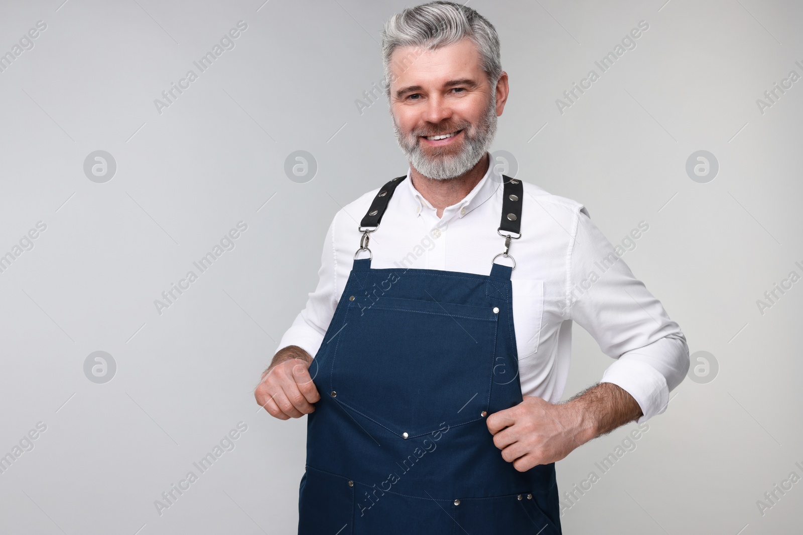 Photo of Happy man wearing kitchen apron on grey background. Mockup for design