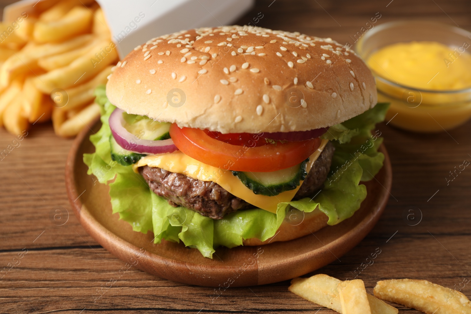 Photo of Delicious burger, sauce and french fries served on wooden table, closeup