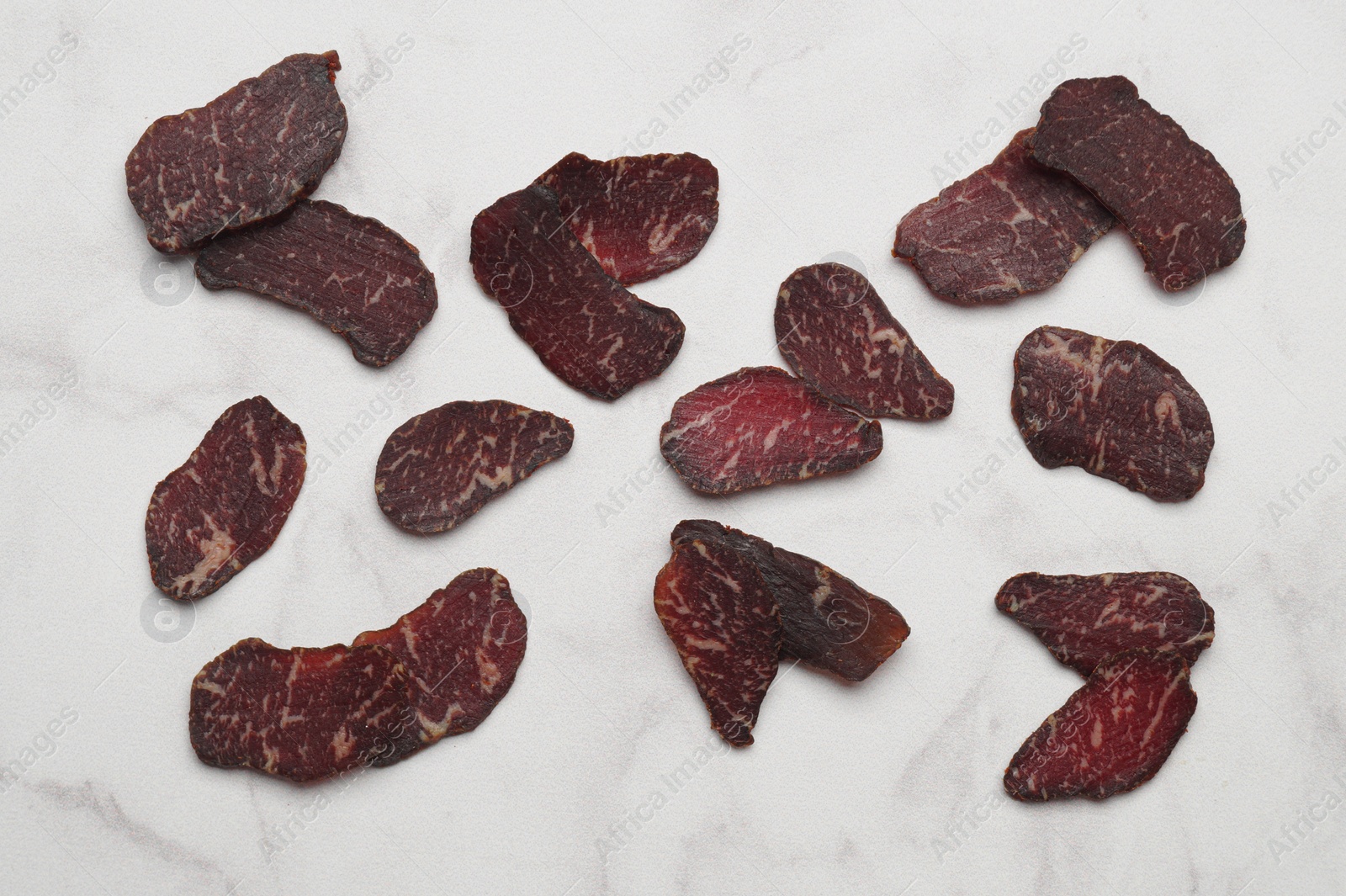 Photo of Delicious beef jerky on white marble table, flat lay
