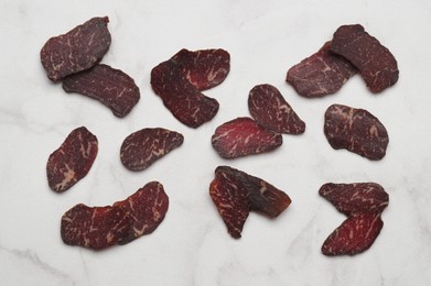 Photo of Delicious beef jerky on white marble table, flat lay
