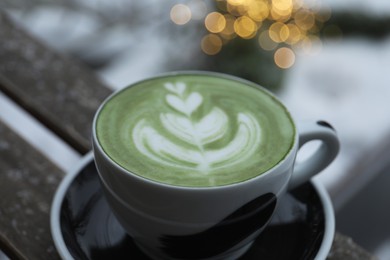 Cup of fresh matcha latte on wooden bench outdoors in winter, closeup
