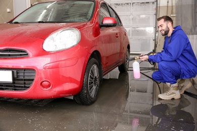 Worker cleaning automobile with high pressure water jet at car wash