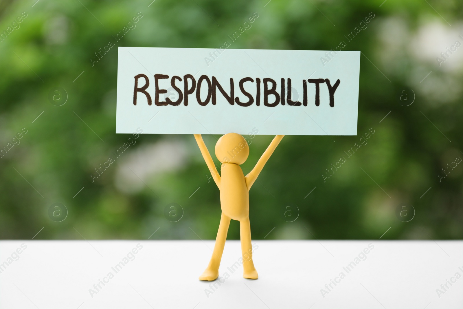 Photo of Plasticine human figure holding card with word Responsibility on white table against blurred background