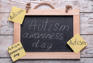 Chalkboard with phrase "Autism awareness day" on wooden background