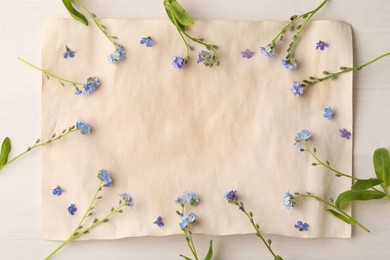 Beautiful Forget-me-not flowers and parchment on white wooden table, flat lay. Space for text