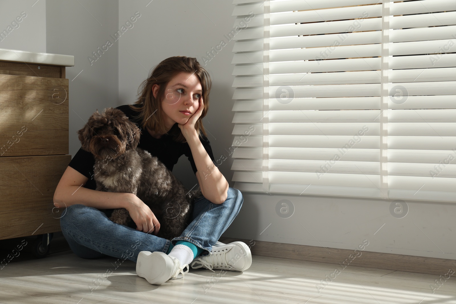 Photo of Sad young woman and her dog sitting on floor indoors, space for text