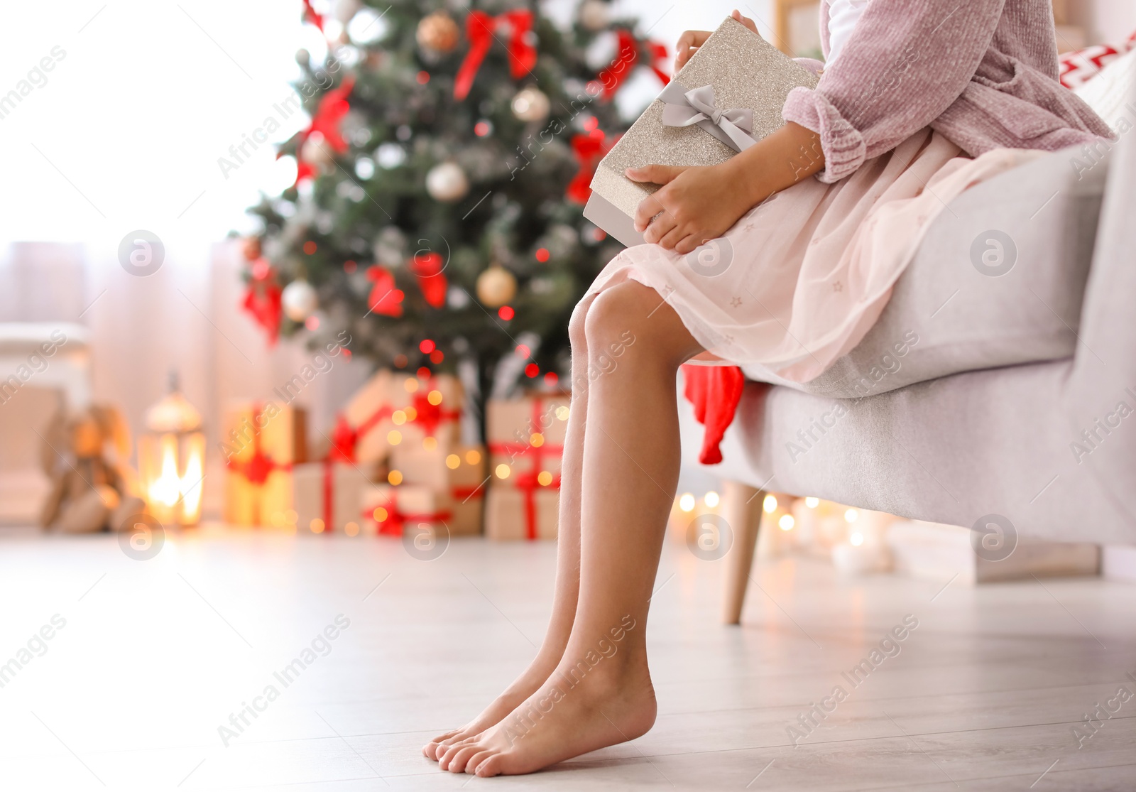 Photo of Cute little child with Christmas gift box sitting on sofa at home