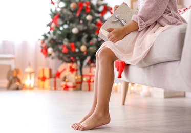 Cute little child with Christmas gift box sitting on sofa at home