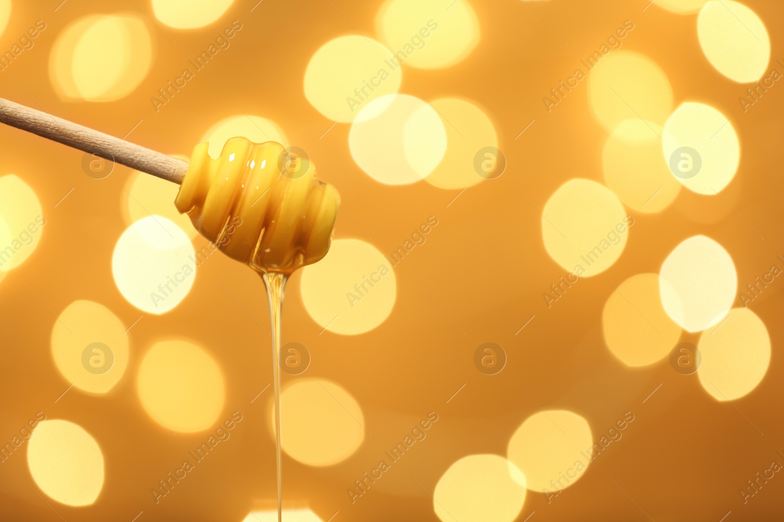 Photo of Dipper with dripping honey against blurred lights. Space for text