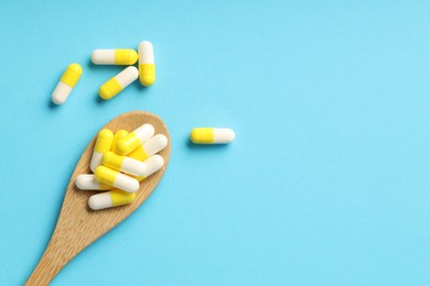 Photo of Many antibiotic pills with wooden spoon and space for text on light blue background, top view. Medicinal treatment