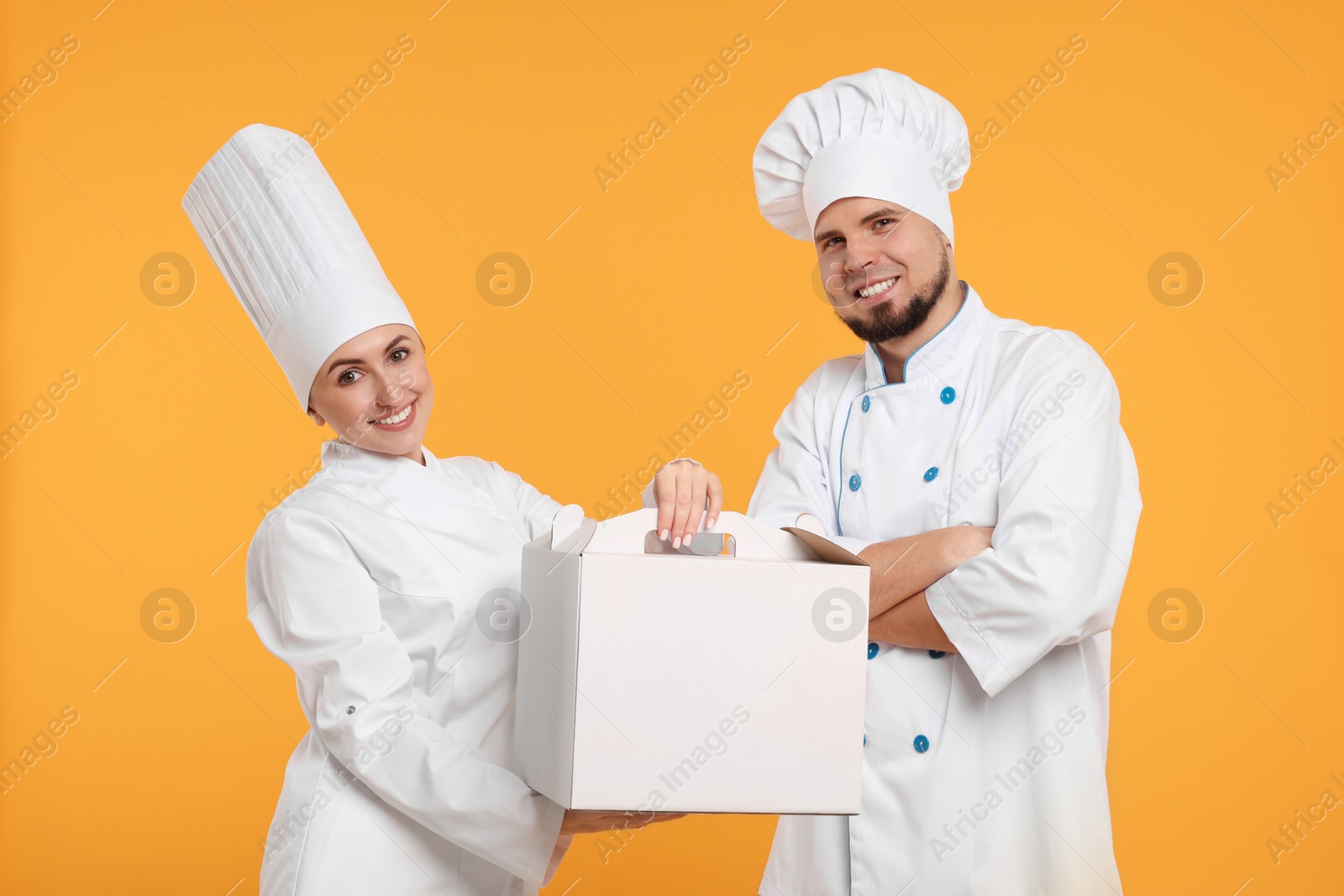 Photo of Happy professional confectioners in uniforms holding cake box on yellow background