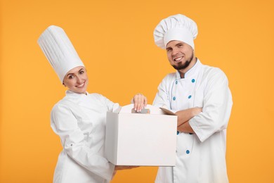 Happy professional confectioners in uniforms holding cake box on yellow background