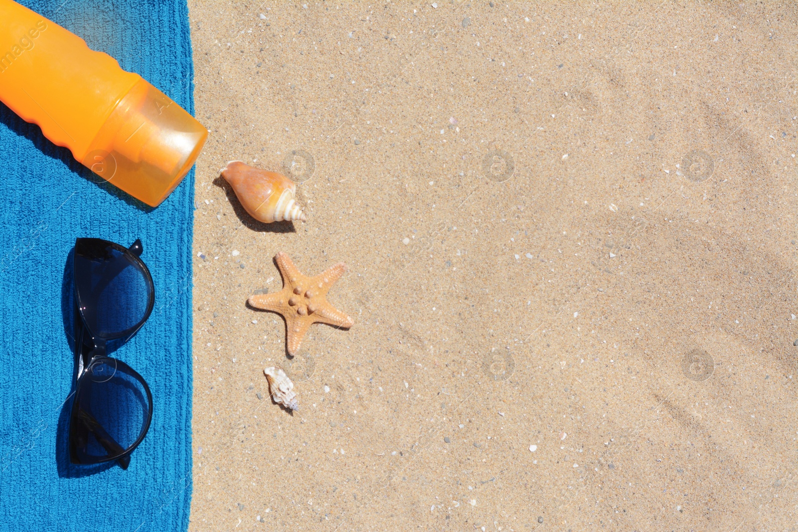 Photo of Stylish sunglasses, bottle of sunblock and blue towel on sand, flat lay with space for text. Beach accessories