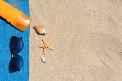 Photo of Stylish sunglasses, bottle of sunblock and blue towel on sand, flat lay with space for text. Beach accessories
