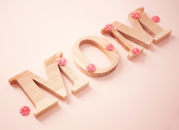 Photo of Word MOM made of wooden letters and flowers on light background. Mother's Day congratulation